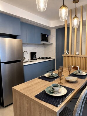Een moderne keuken met een roestvrijstalen koelkast, een magnetron en een gasfornuis. Er staat een houten eettafel met borden en glazen, gedekt voor een maaltijd.