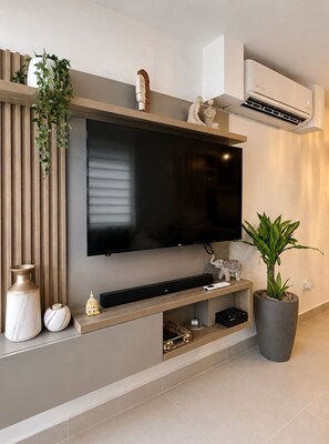Ein modernes Wohnzimmer mit einem Wand-Fernseher, Holzvertäfelung, einer Blumentopfpflanze und einer großen Vase.