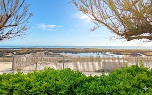A fenced area with a view of the ocean, a sandy beach, and a rocky shoreline. - Seaside house with cliff views (Piriac-sur-Mer)