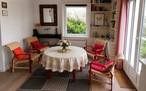 A dining area with a round table, chairs, a vase of flowers, a mirror, and a bookshelf. - Seaside house with cliff views (Piriac-sur-Mer)