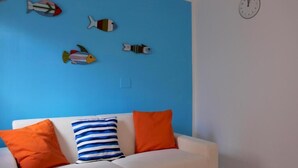 Un sofá blanco con tres almohadones, una pared azul y un reloj.