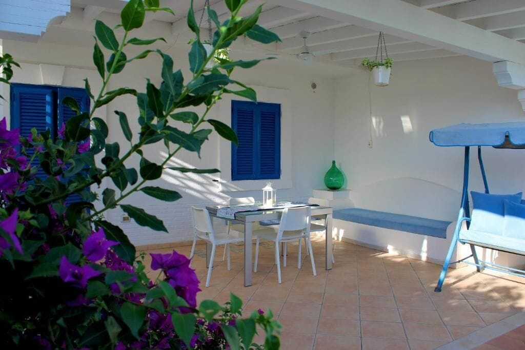 Un espace patio avec une table et des chaises, une plante suspendue et un banc bleu.
