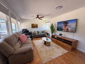 Ein Wohnzimmer mit einer Couch, einem Couchtisch, einem Fernseher und einem Deckenventilator.
