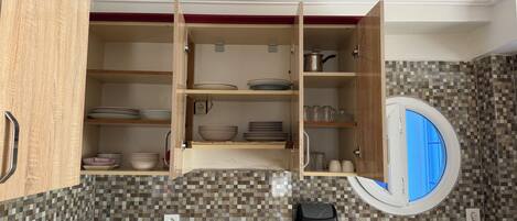 A kitchen with open cabinets, a tiled backsplash, a window, and a trash bin.