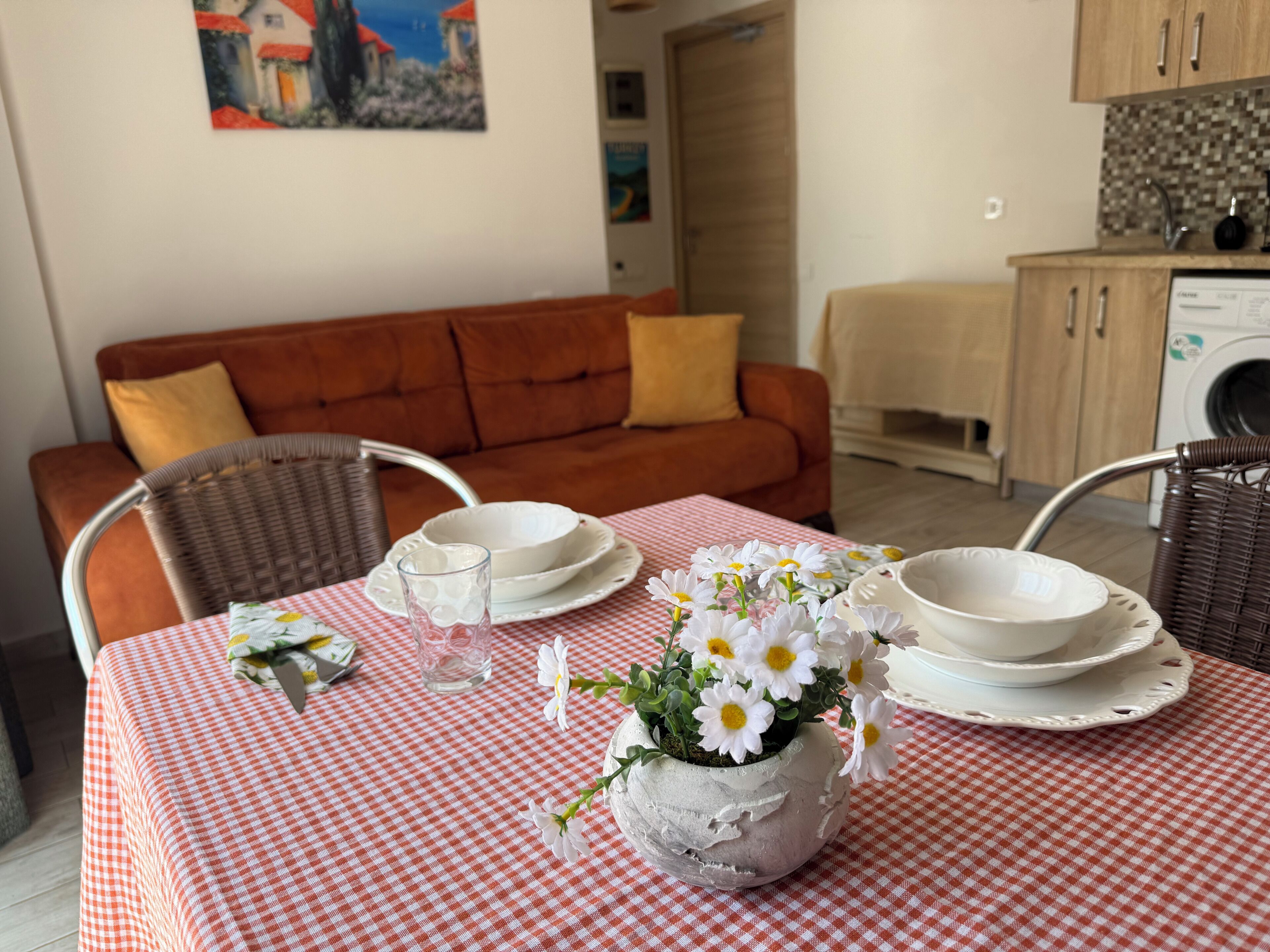 A dining table with a checkered tablecloth, white plates, a glass, and a flower vase.