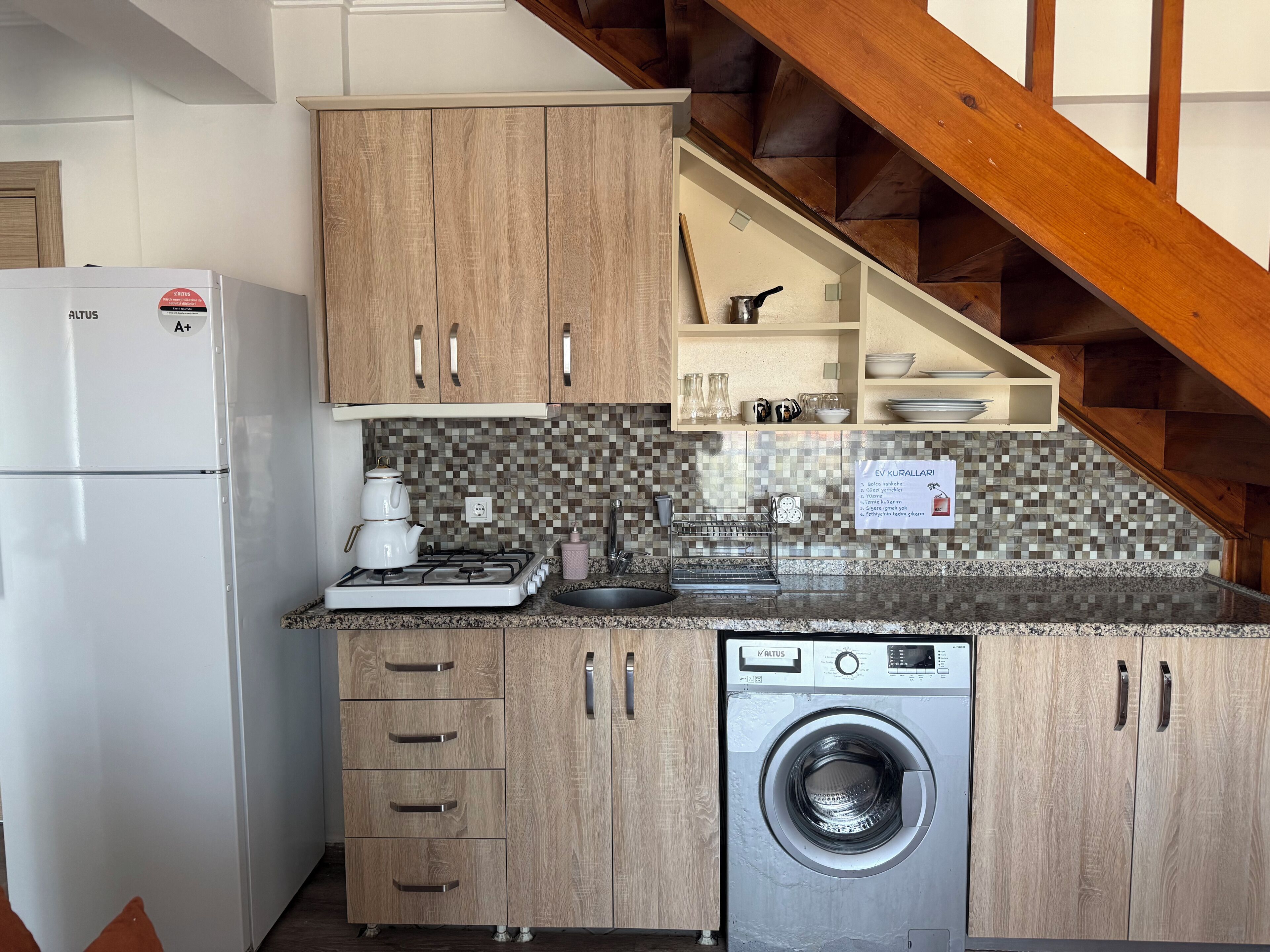 A compact kitchen with wooden cabinets, a built-in washing machine, a stove, and a refrigerator.
