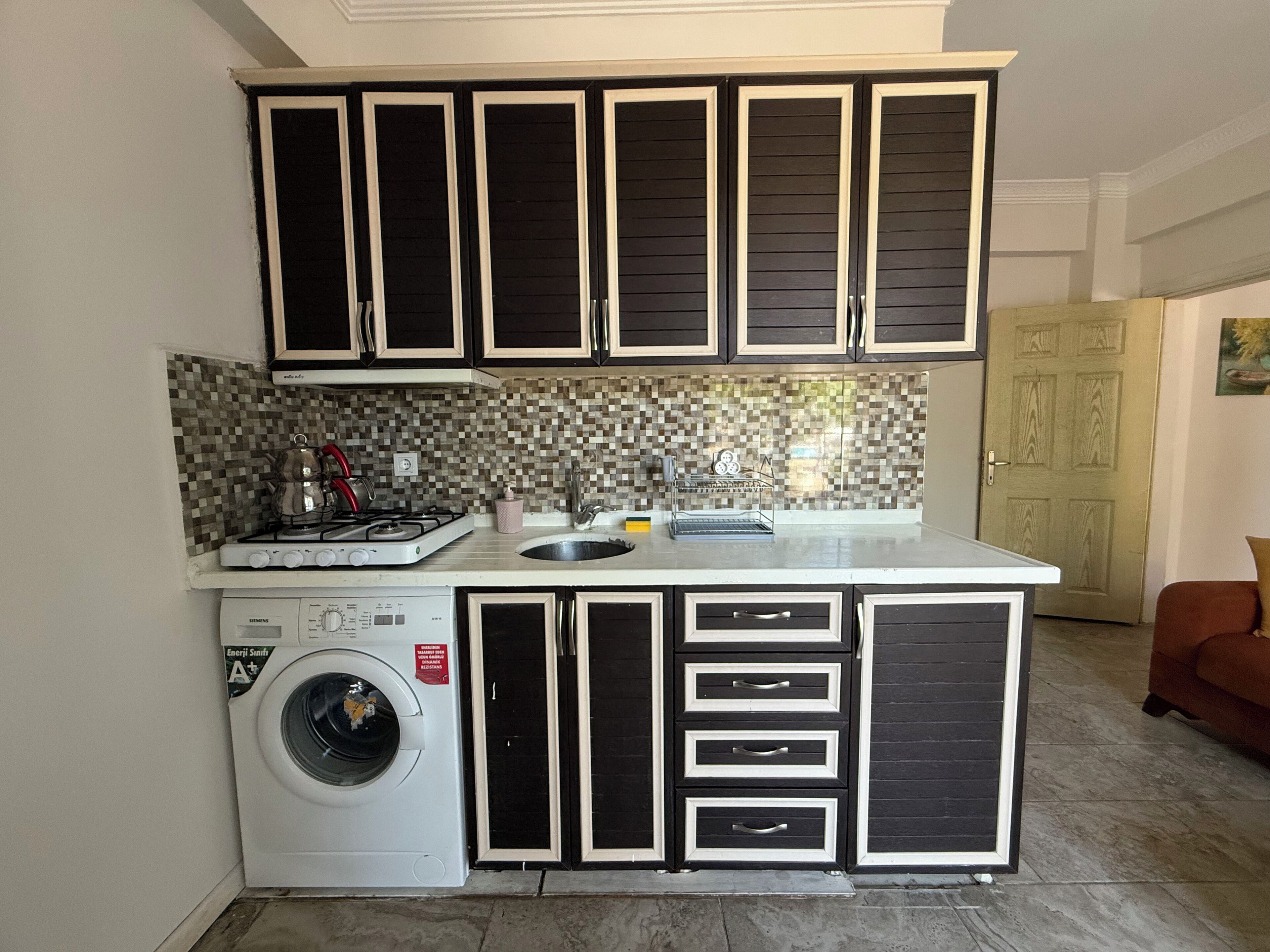 A compact kitchen with a washing machine, a sink, and a stove.