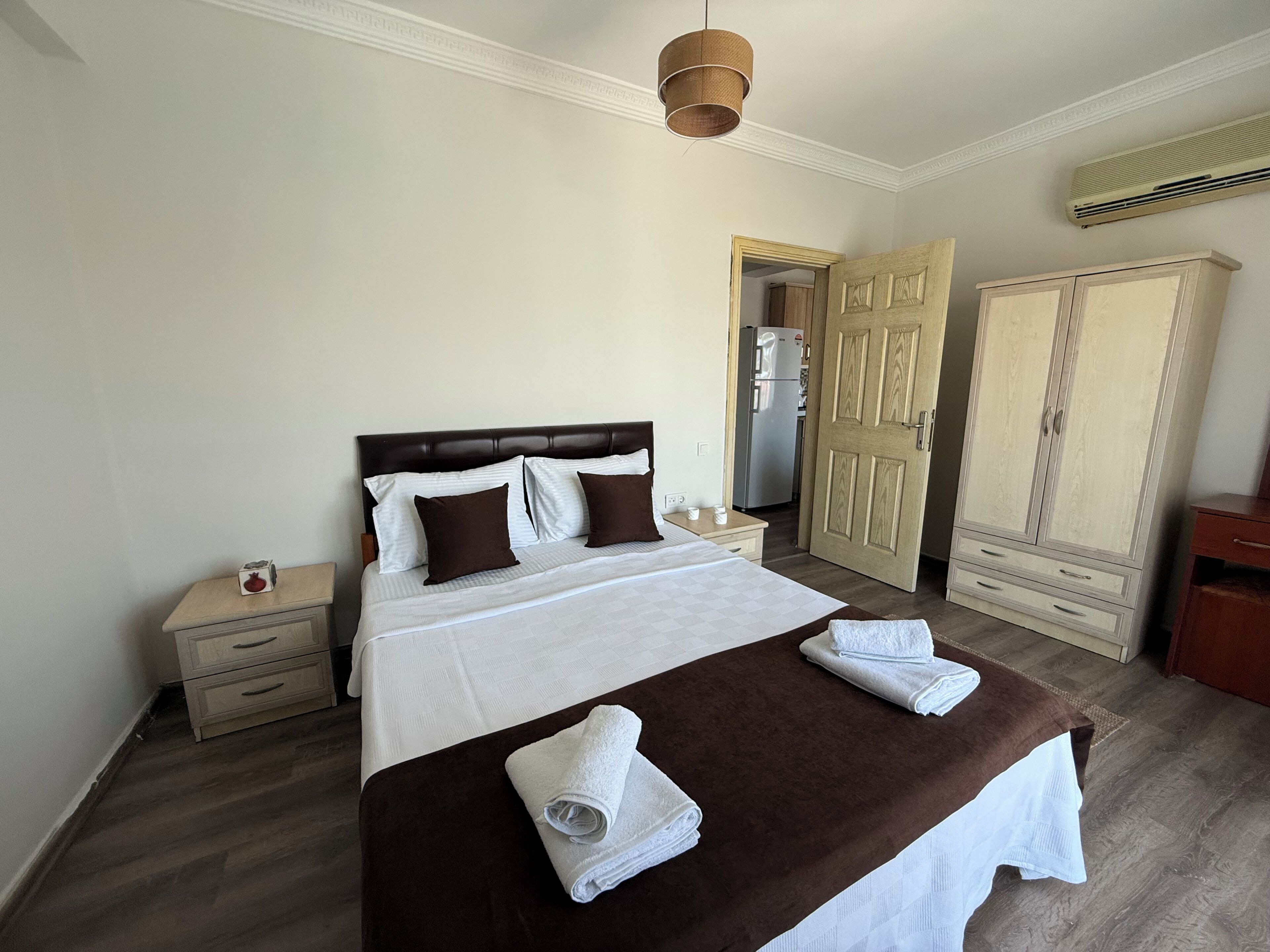 Habitación de hotel con una cama, una mesita de noche, un armario y una puerta abierta que da a una cocina.