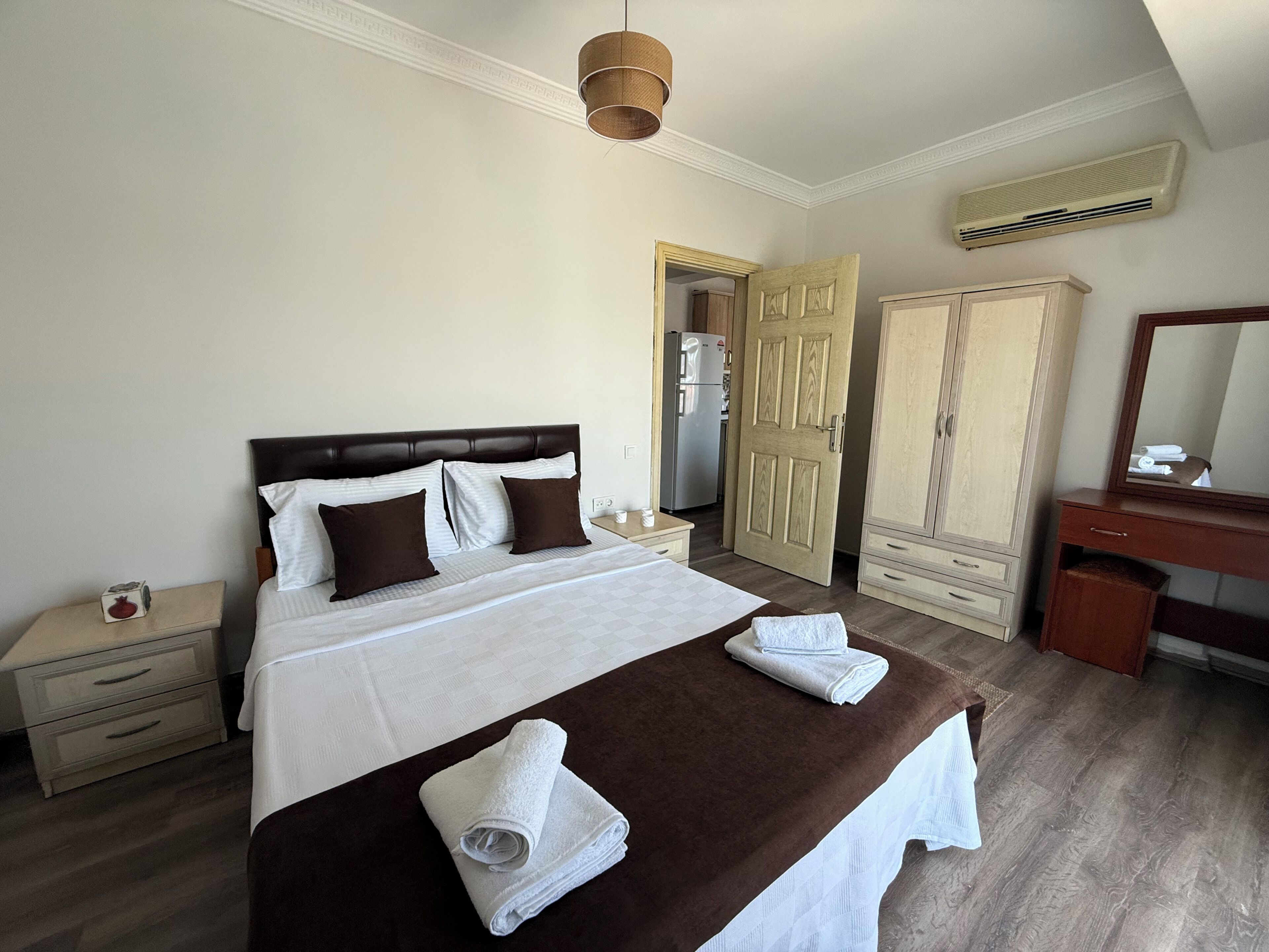 A hotel room with a bed, a nightstand, a wardrobe, a mirror, and an air conditioning unit.