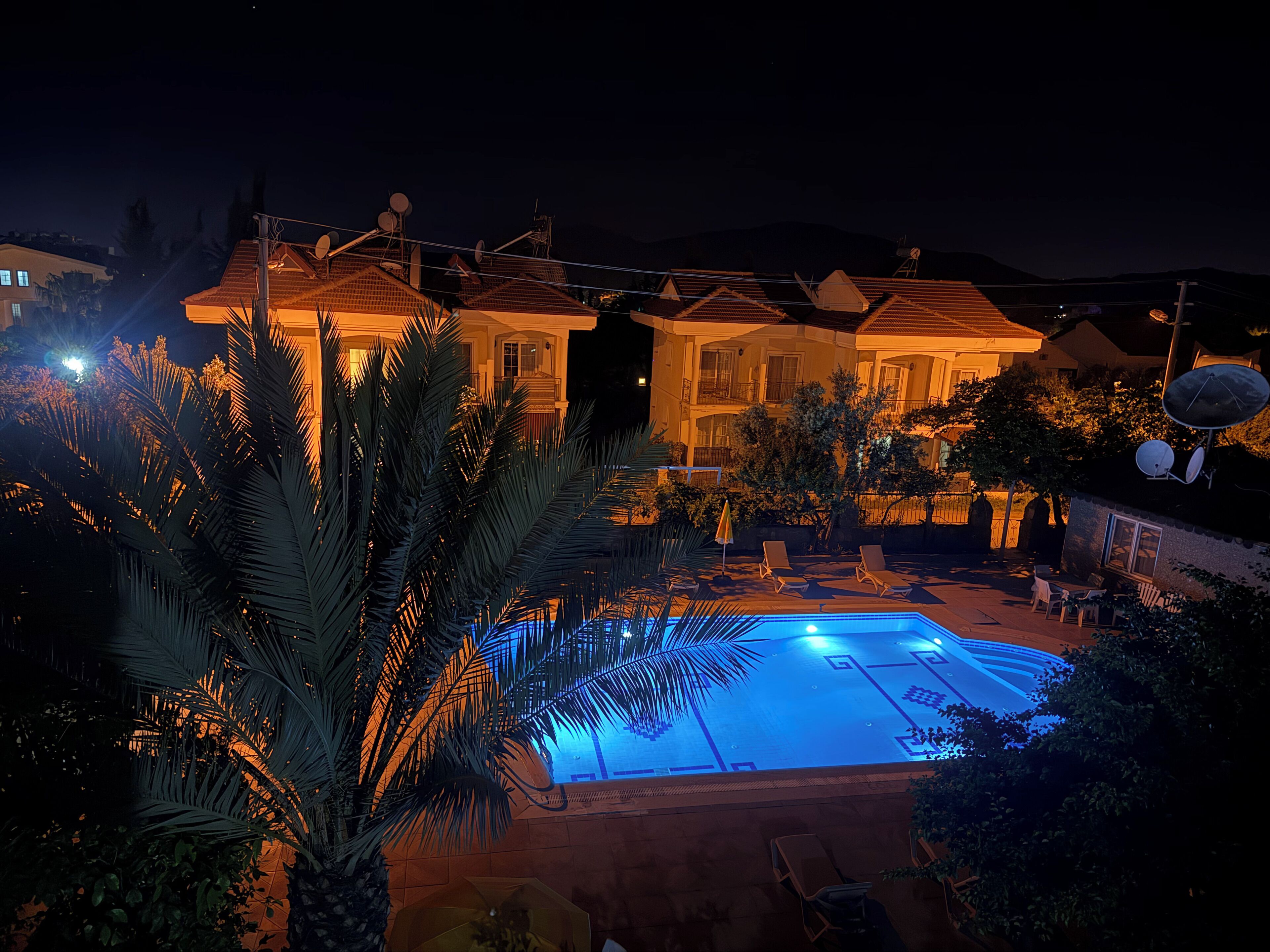 A large house with a swimming pool, surrounded by palm trees and satellite dishes.
