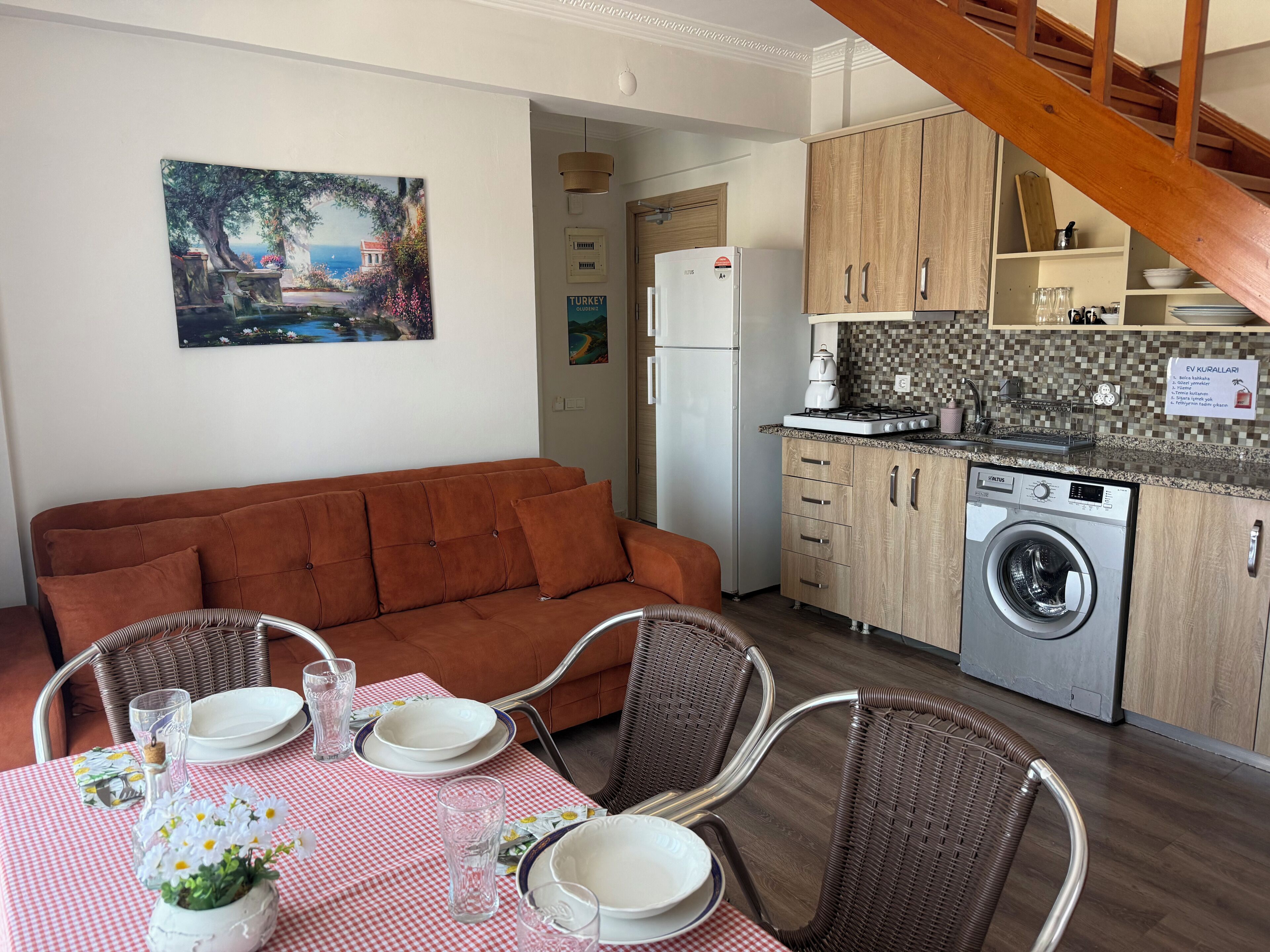 A compact living space with a sofa, dining table, chairs, a washing machine, and a kitchen area.