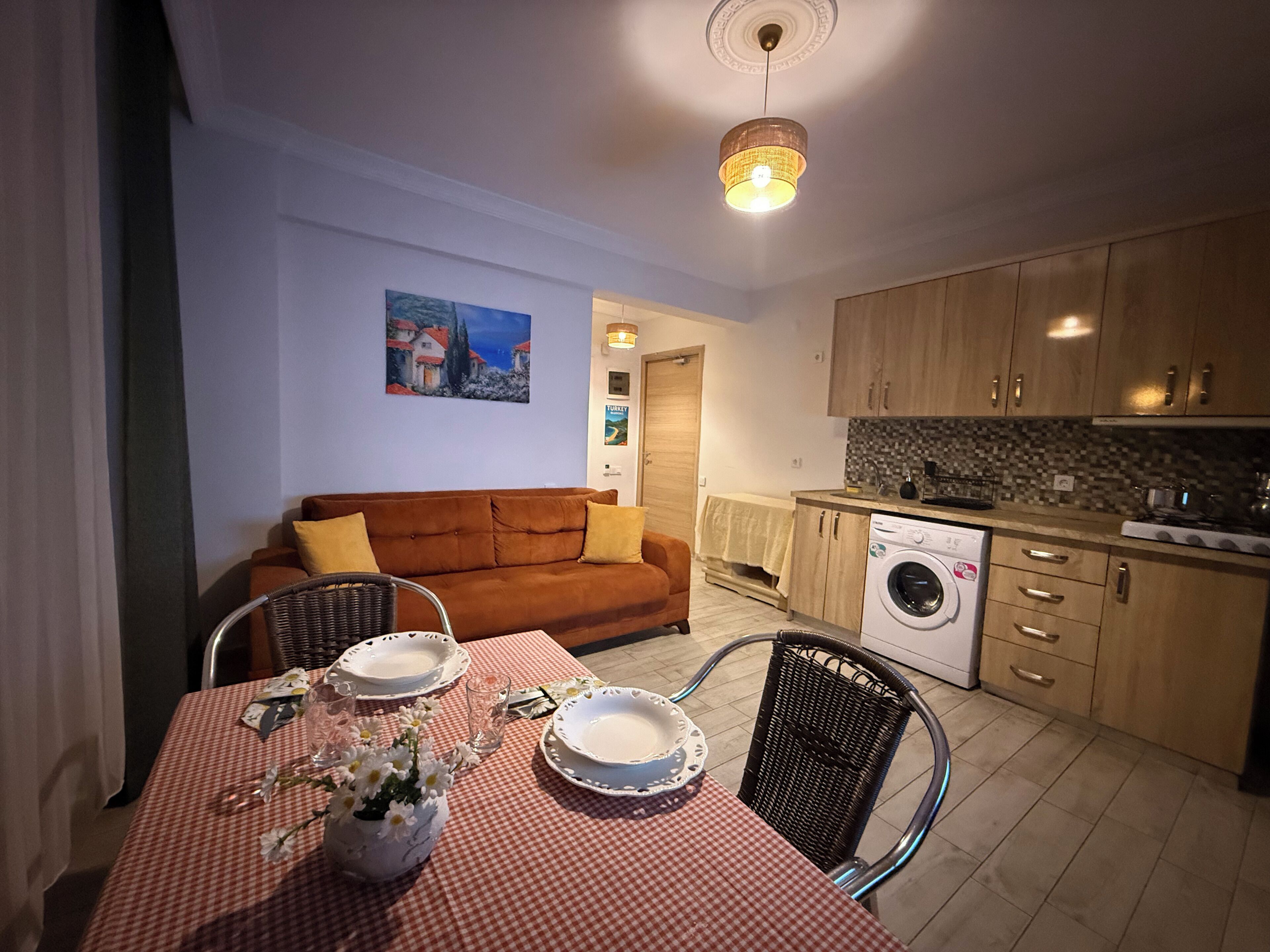 Un espace de vie compact comprenant une table à manger pour deux personnes, un canapé, un lave-linge et une petite cuisine.