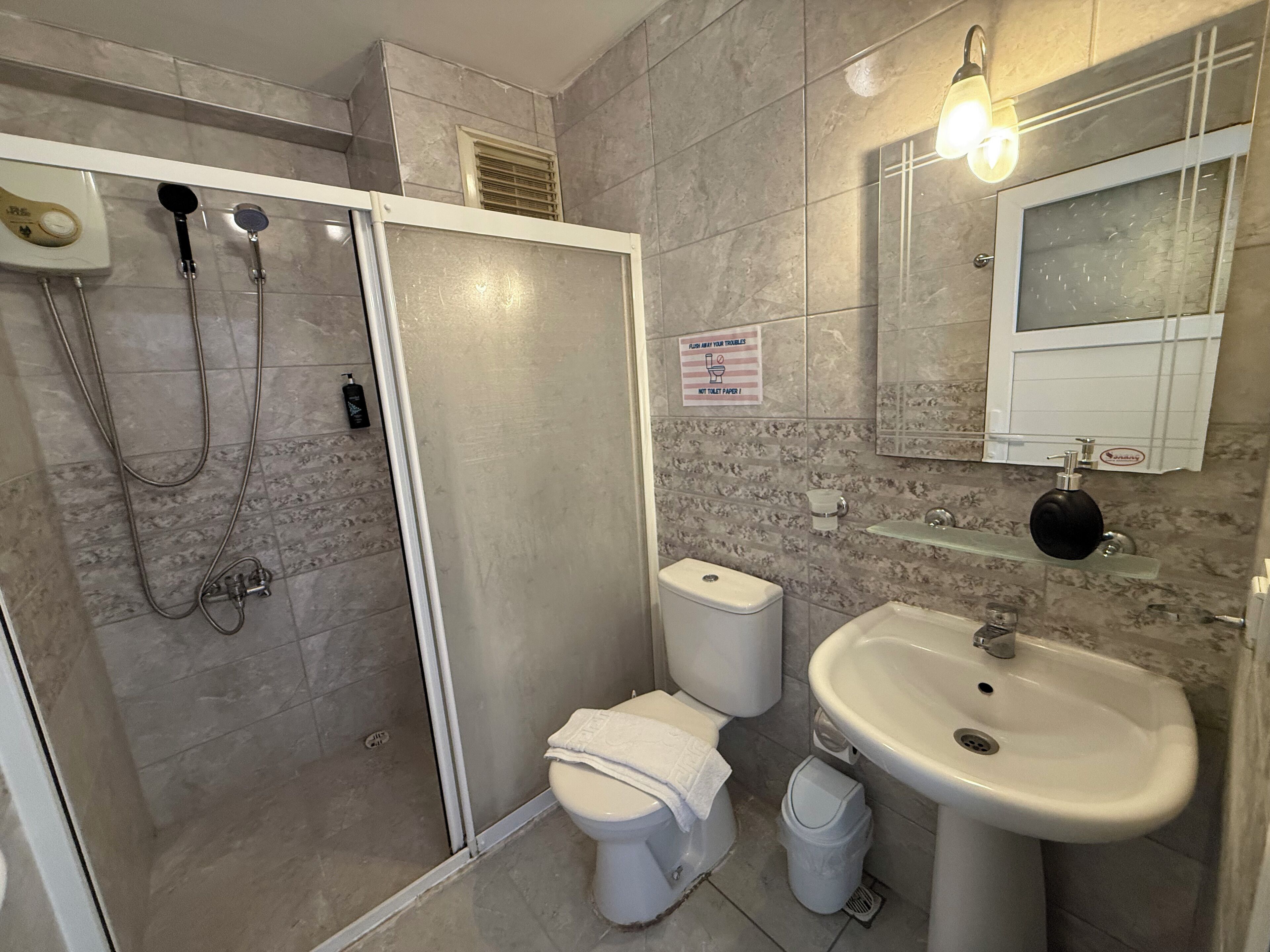 A bathroom with a shower, toilet, sink, and a mirror.