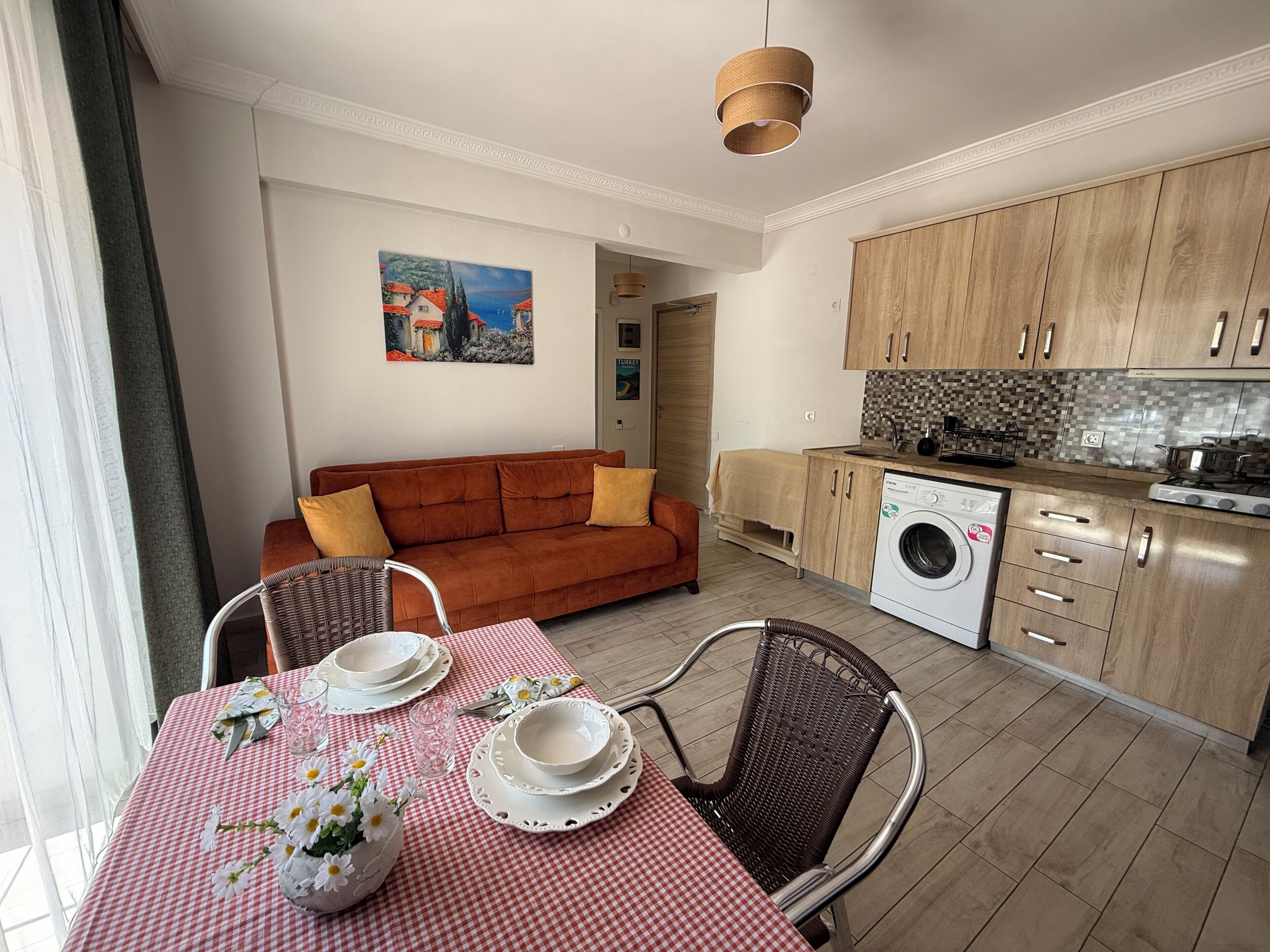 En kompakt bolig med spiseplads, sofa, tekøkken og vaskemaskine.