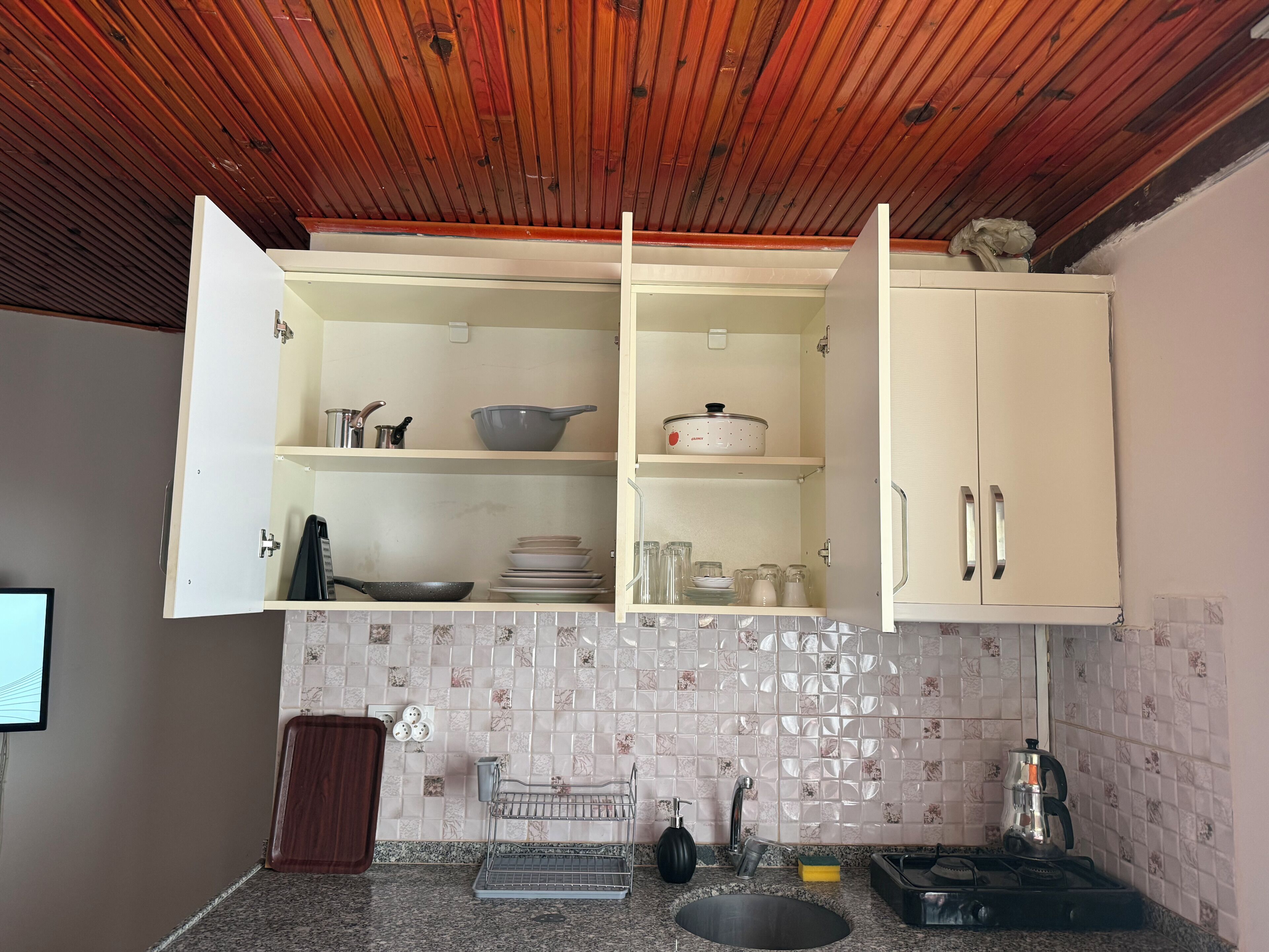 Cuina amb sostre de fusta, armaris blancs i un rebedor de rajola.
