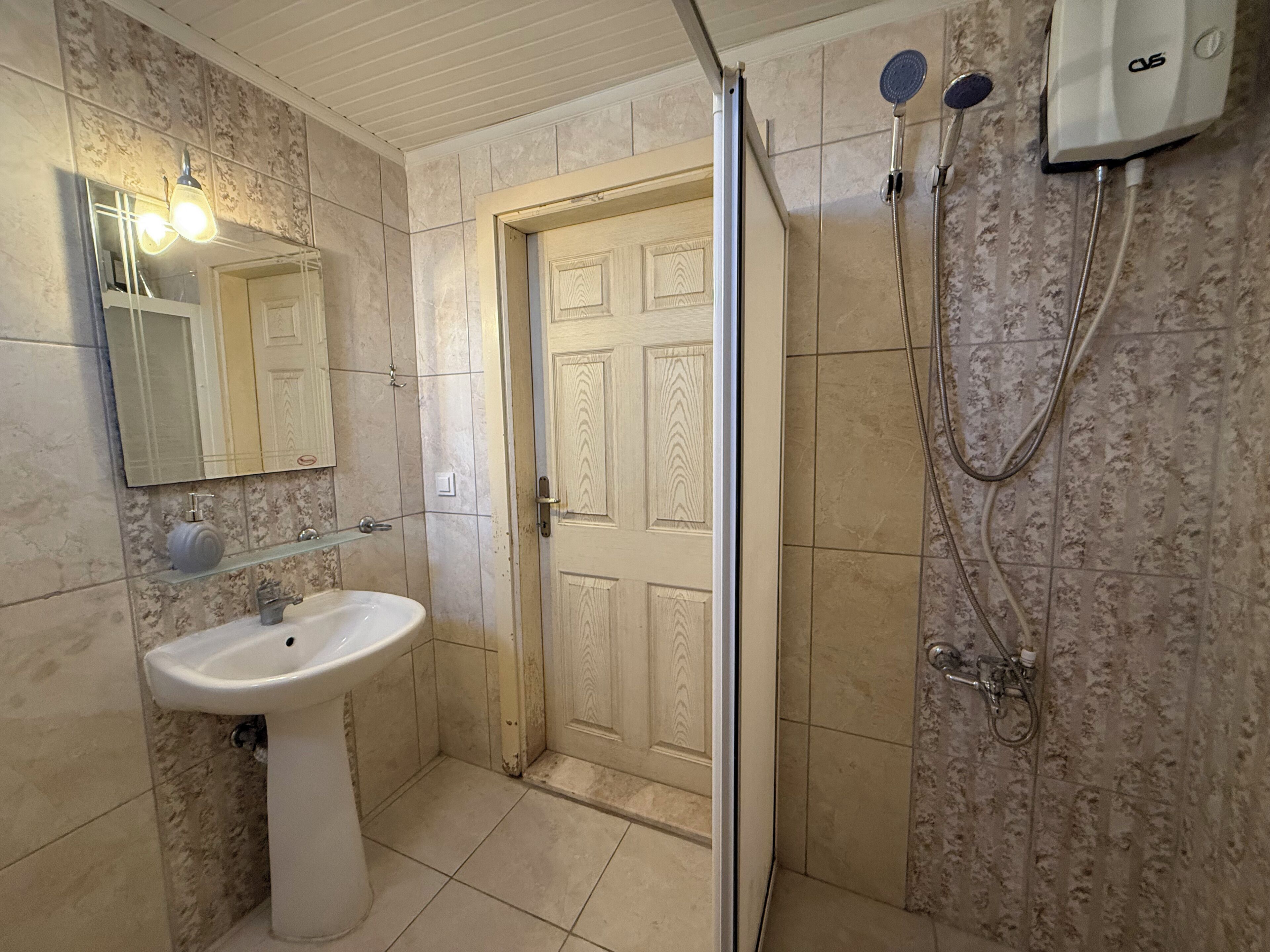Une salle de bain avec un lavabo, un miroir, une porte et une douche.