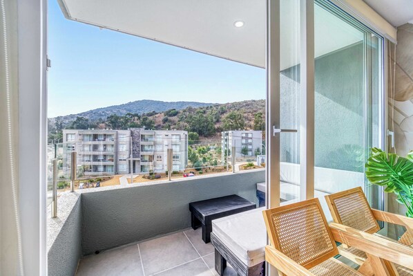 Ein Balkon mit Blick auf Gebäude und Hügel, ein Tisch, zwei Stühle und ein Blumentopf.
