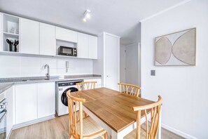Eine moderne Küche mit weißen Schränken, einer Mikrowelle, einem Geschirrspüler und einem Holztisch mit vier Stühlen.