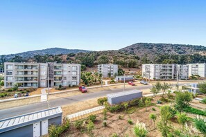 A residential area with modern apartment buildings, a road, and a hilly landscape in the background.