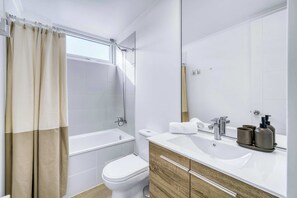 A modern bathroom with a bathtub, toilet, and vanity with a mirror.