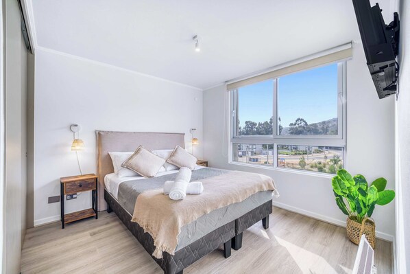 A bedroom with a bed, bedside tables, a window, and a plant.