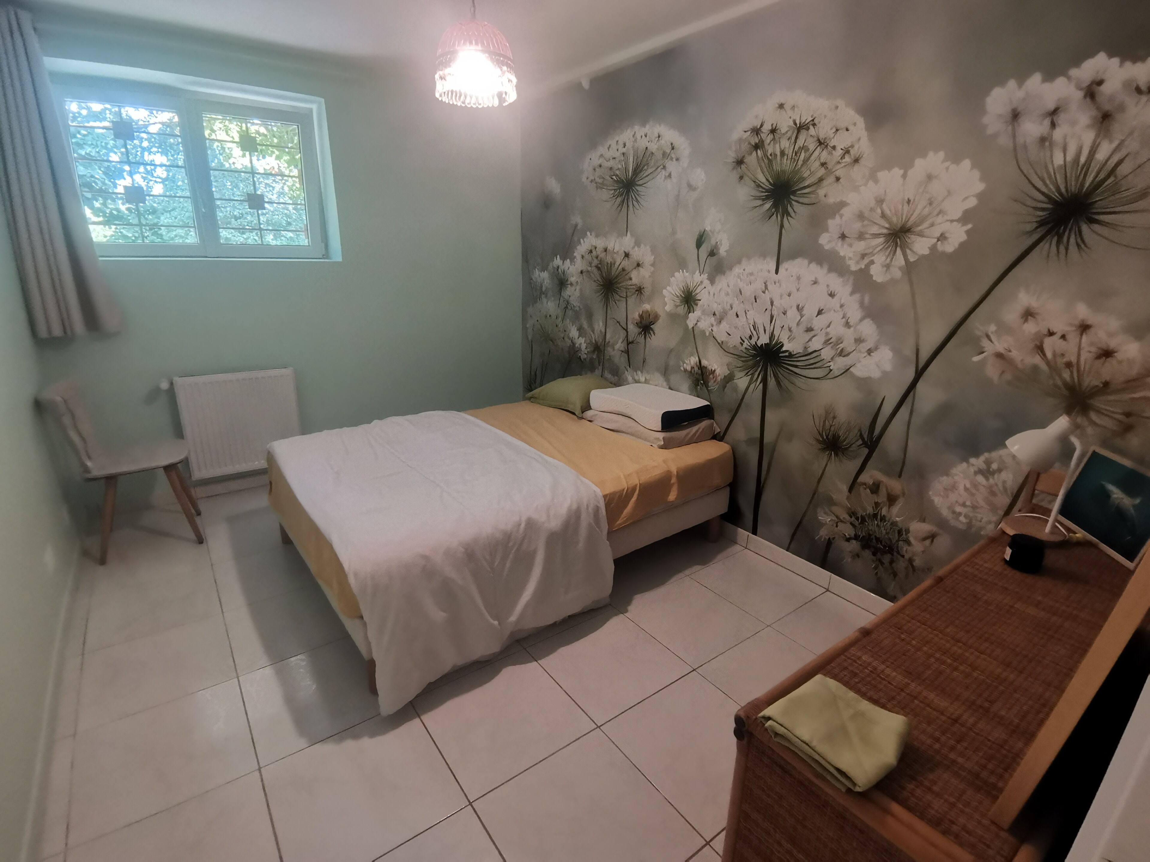 Een slaapkamer met een bed, een stoel, een bureau met een lamp en een muurschildering.