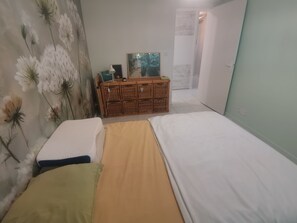 Une chambre à coucher avec un lit, une commode et un mur recouvert d’un papier peint à motifs floraux.