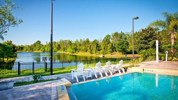 Una piscina con sillas reclinables blancas y vistas a un lago y árboles.