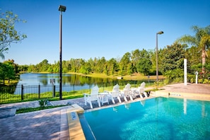 Ein Pool mit weißen Liegestühlen und Blick auf einen See und Bäume.