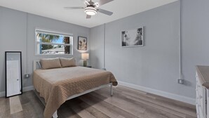 A bedroom with a bed, ceiling fan, window, artwork, and a dresser. - Dune Your Thing C (Fort Myers Beach)