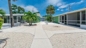 A courtyard with a pathway, palm trees, and a building with large windows. - Dune Your Thing C (Fort Myers Beach)