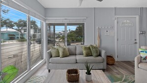 Una sala de estar moderna con un sofá gris, un ventilador de techo y vistas a través de amplios ventanales correderas.