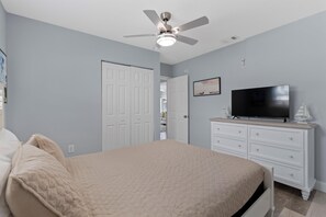 A bedroom with a bed, a ceiling fan, a TV, and a dresser.