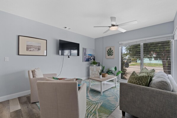 A living room with a sofa, armchair, coffee table, and a TV mounted on the wall.