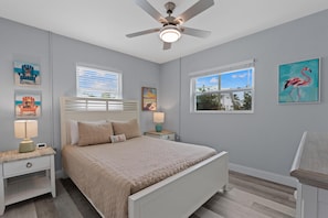 A bedroom with a bed, nightstands, a ceiling fan, and artwork on the walls.