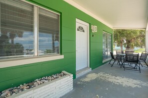 A green building with a white door, large windows, and a patio area with outdoor furniture.