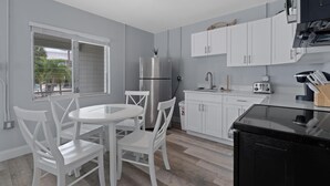 Una cocina moderna con armarios blancos, un refrigerador de acero inoxidable, una mesa redonda de comedor con sillas blancas y una encimera negra.