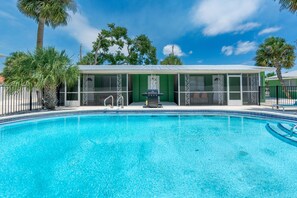 A swimming pool with a covered area, palm trees, and a clear sky. - Dune Your Thing A (Fort Myers Beach)