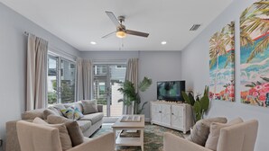 A living room with a sofa, armchairs, a coffee table, a TV, and a ceiling fan. - Dune Your Thing A (Fort Myers Beach)