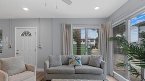 A living room with a sofa, a coffee table, and a large window with curtains. - Dune Your Thing A (Fort Myers Beach)