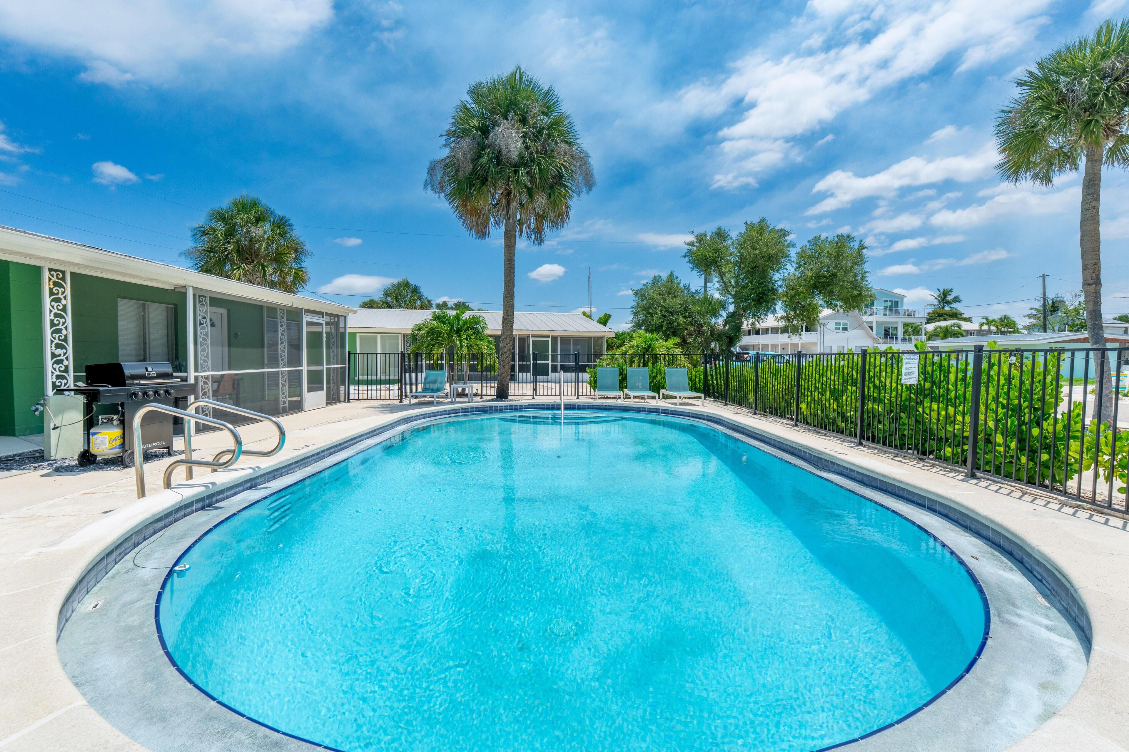 A swimming pool with a clear blue water, surrounded by a fence, and palm trees in the background.