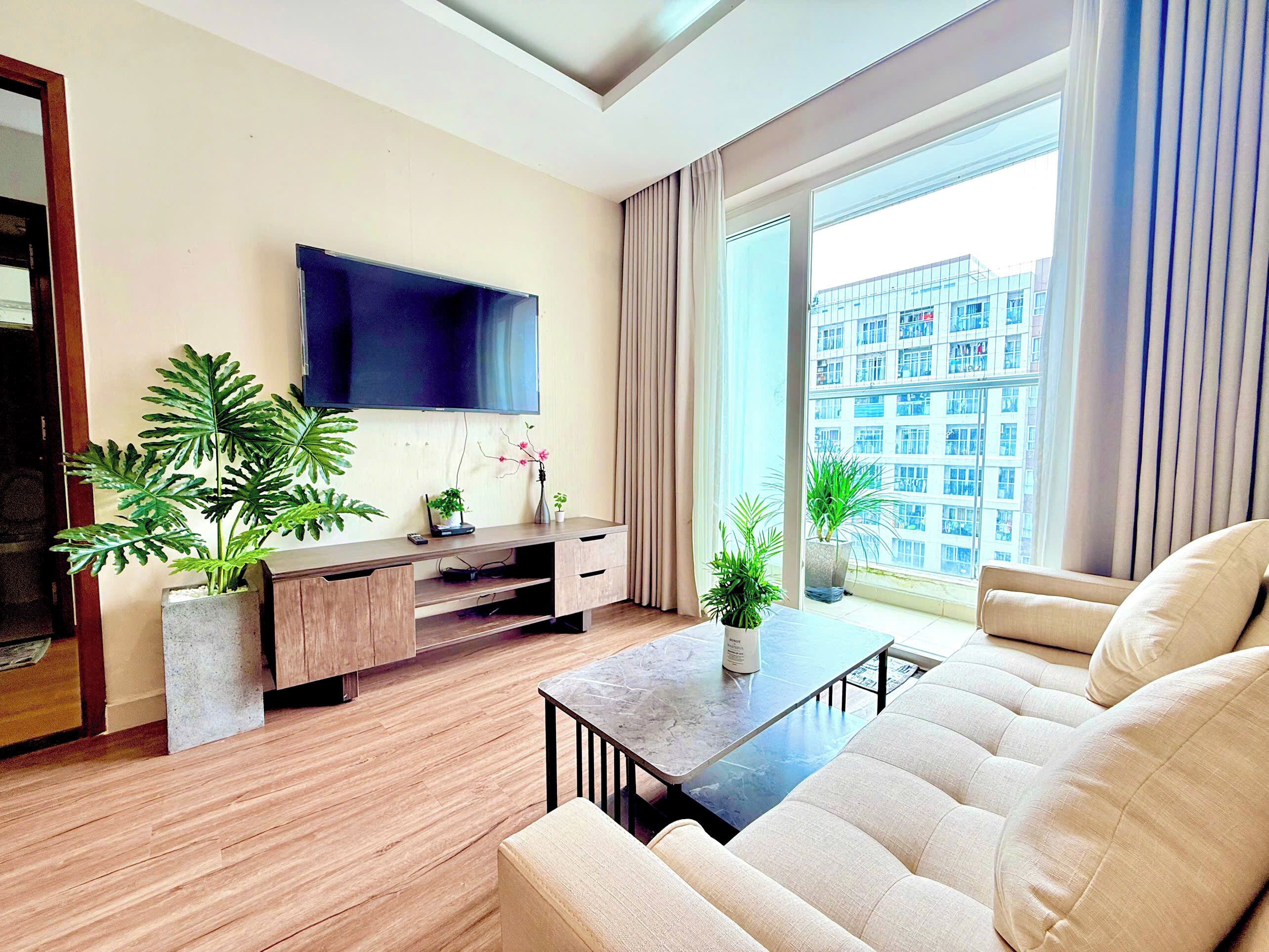Una sala de estar moderna con televisor de pantalla plana, piso de madera, un sofá, una mesa de centro y plantas en macetas.