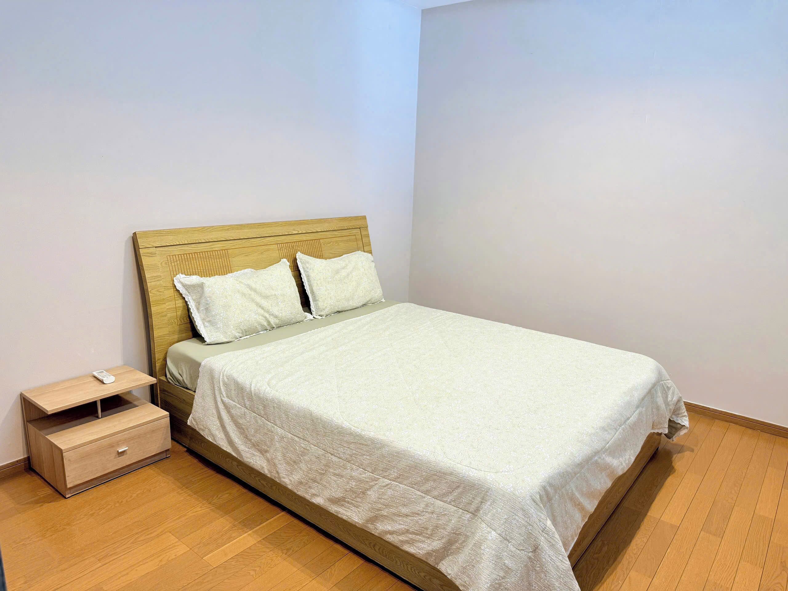 A single bed with a wooden headboard, a bedside table with a drawer, and a small shelf.