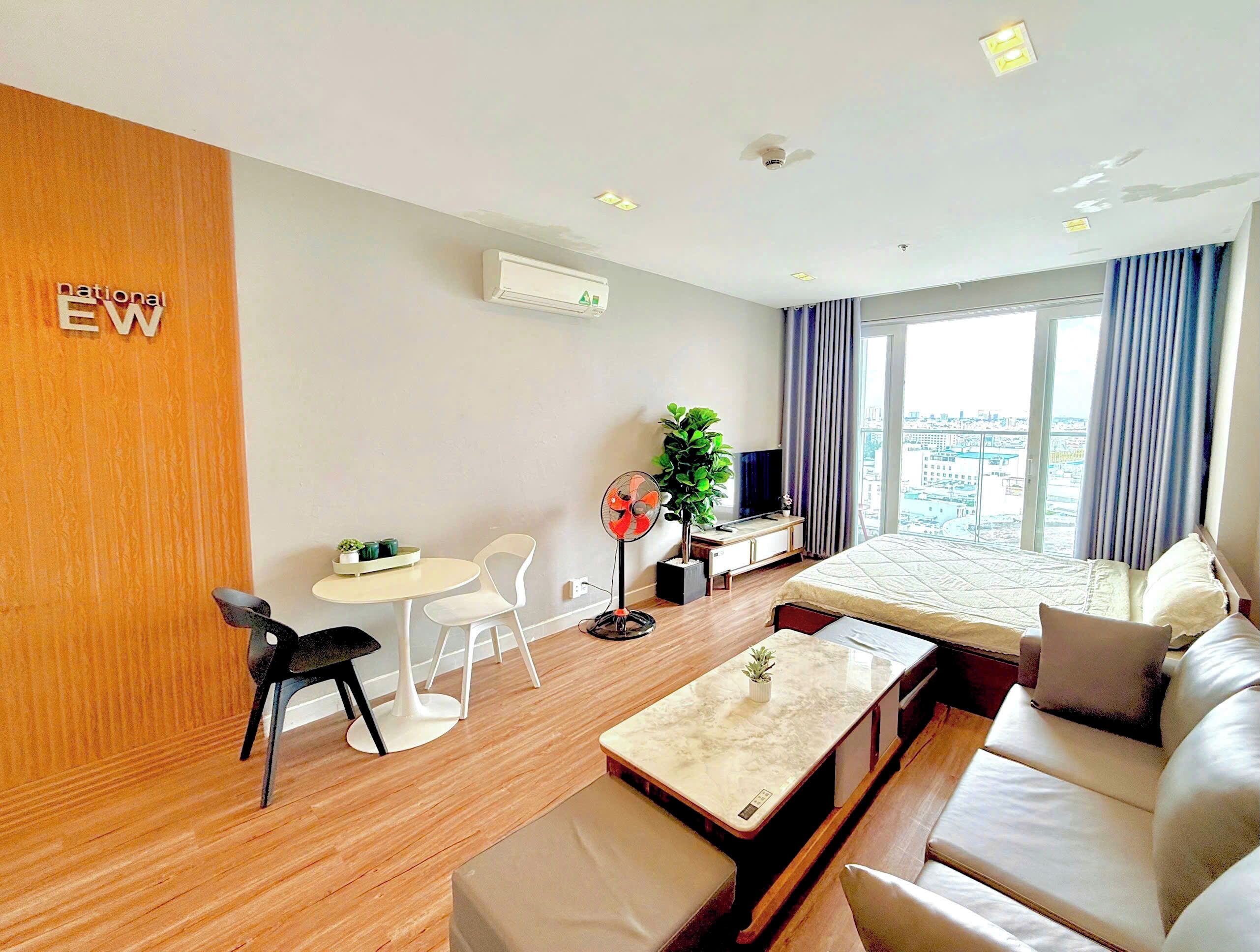 Ein Hotelzimmer mit Bett, Sofa, Esstisch, Fernseher, Pflanze und Blick auf die Stadt.