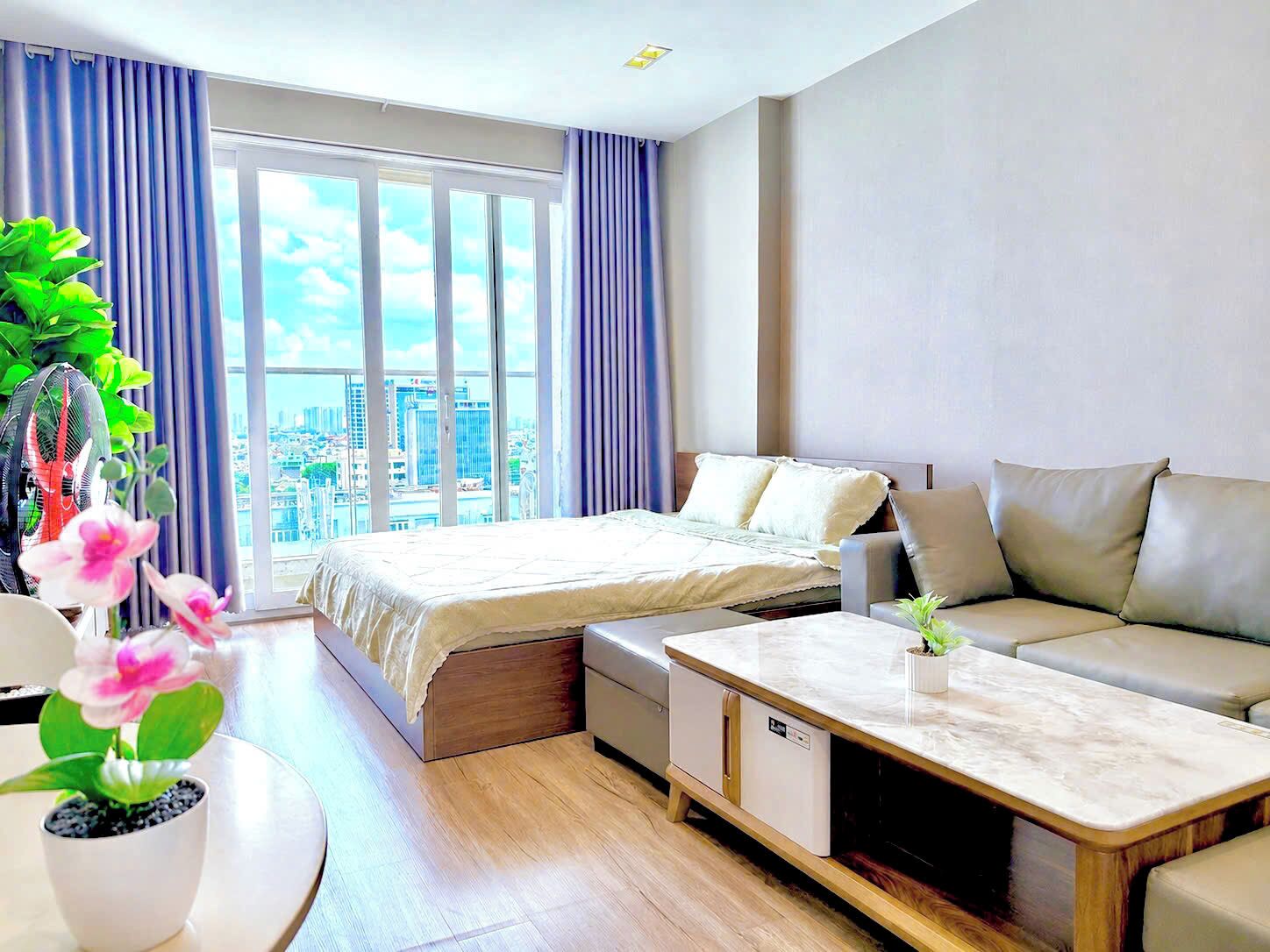Une chambre d’hôtel moderne équipée d’un lit, d’un canapé et d’une table à manger, de grandes fenêtres avec des rideaux et offrant une vue sur la ville.