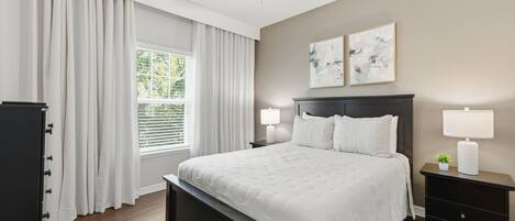 A bedroom with a bed, a nightstand, a dresser, a ceiling fan, and a window with curtains.