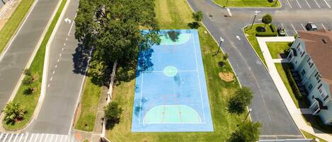 An aerial view of a residential area with a basketball court surrounded by trees and a road.