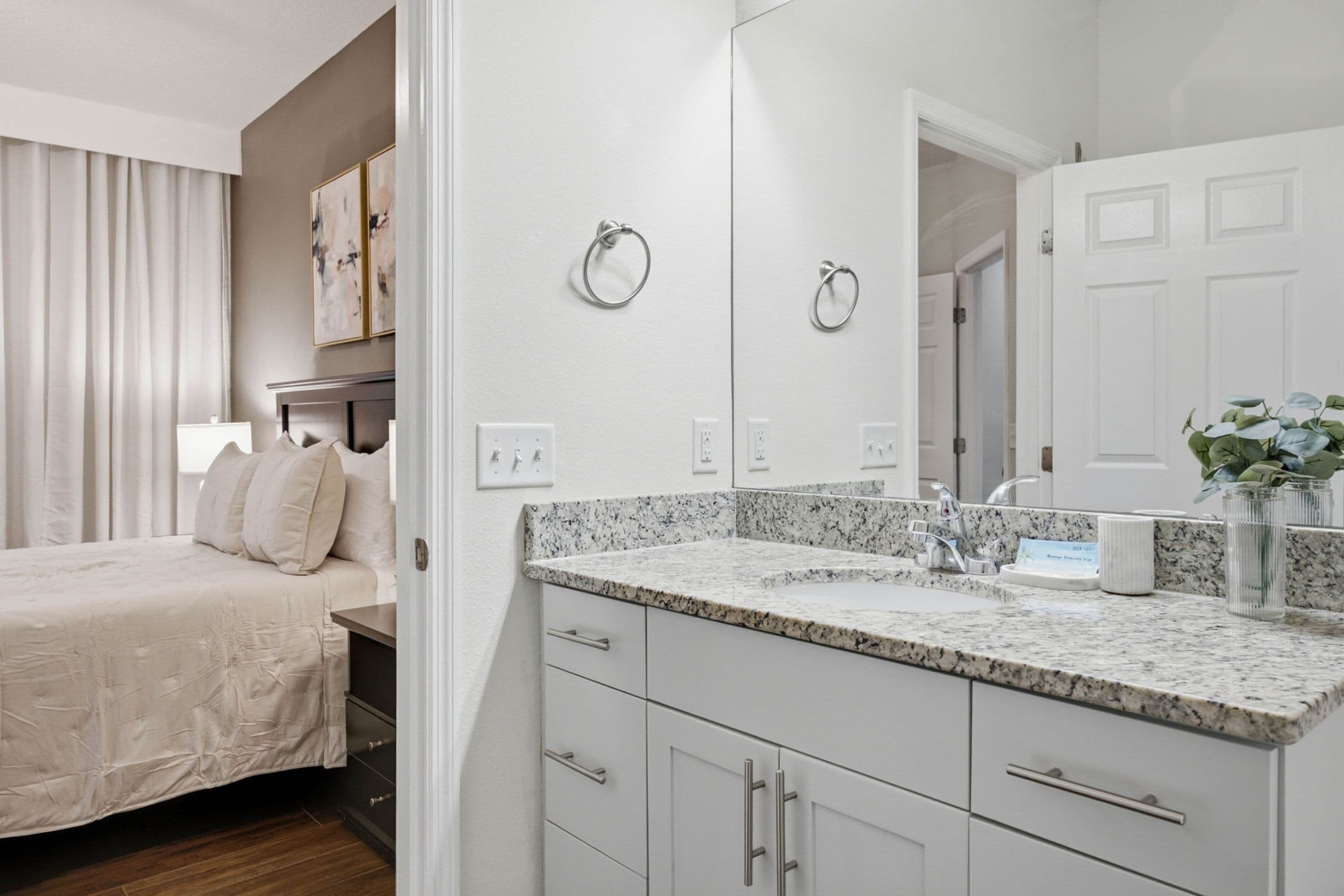 A modern bathroom with a granite countertop, a large mirror, and a white sink.