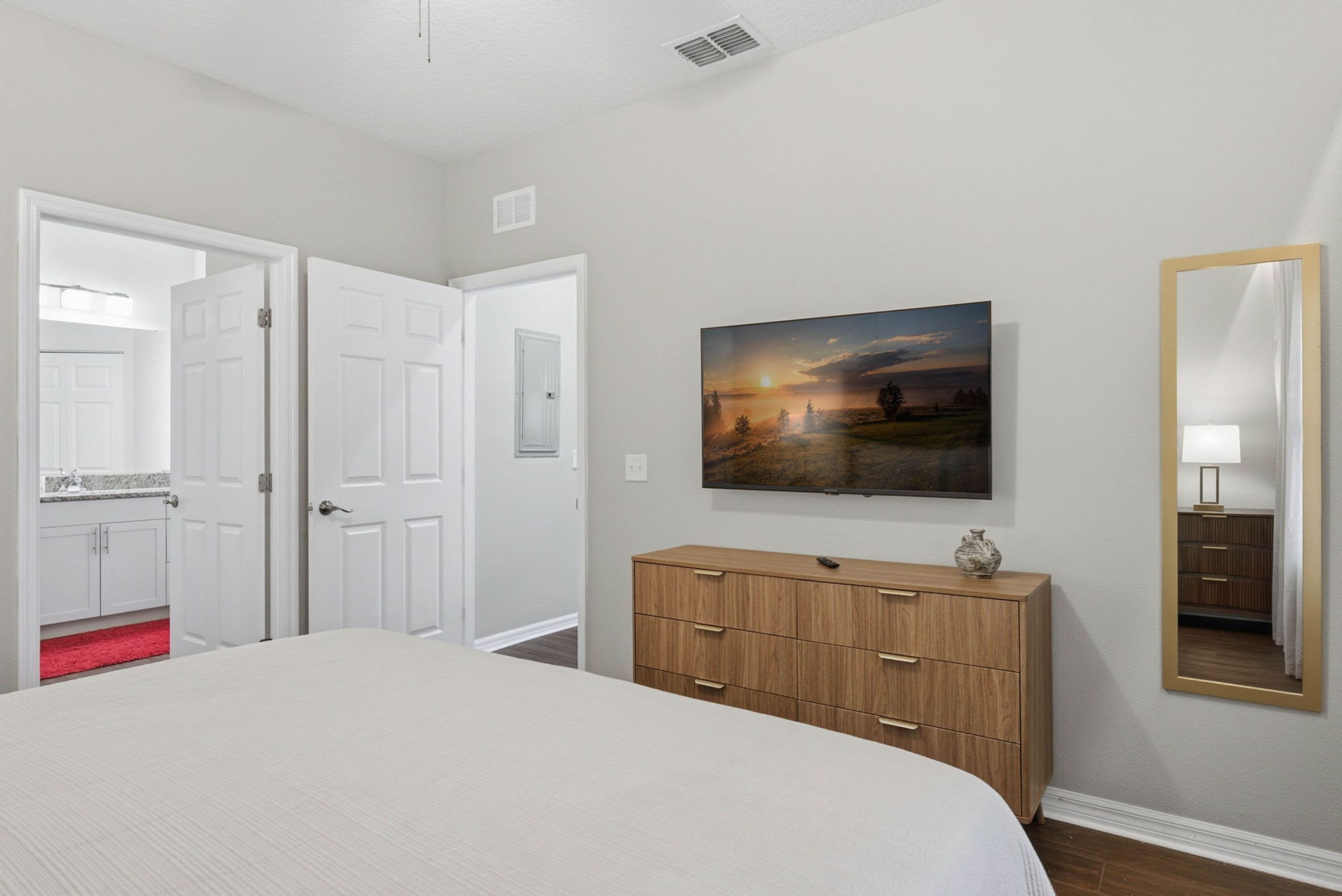 A bedroom with a bed, a dresser, a painting, and a mirror.