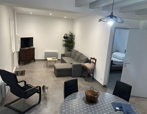 Una sala de estar moderna con un sofá, una mesa de comedor, un televisor y una planta.